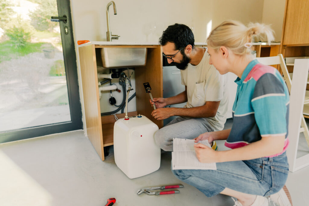 Homeowners inspecting an under-sink water system while following maintenance instructions.